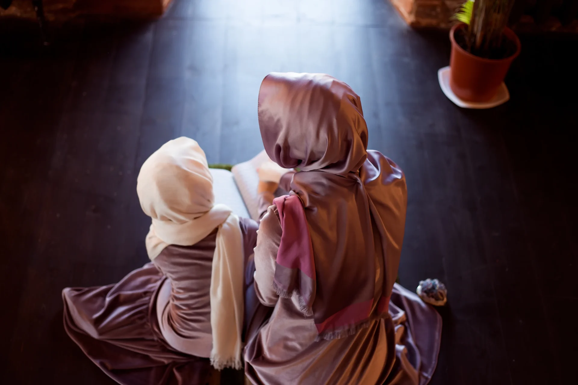 A woman sitting on the floor with her head wrapped in a blanket.