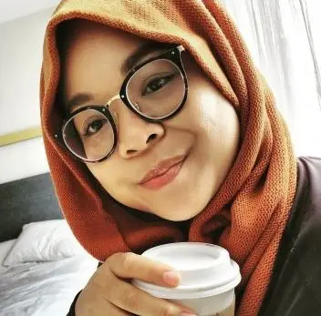 A woman in glasses and a head scarf holding a cup.