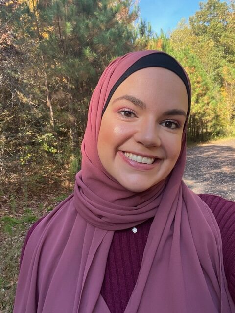 A woman wearing a hijab standing in front of trees.