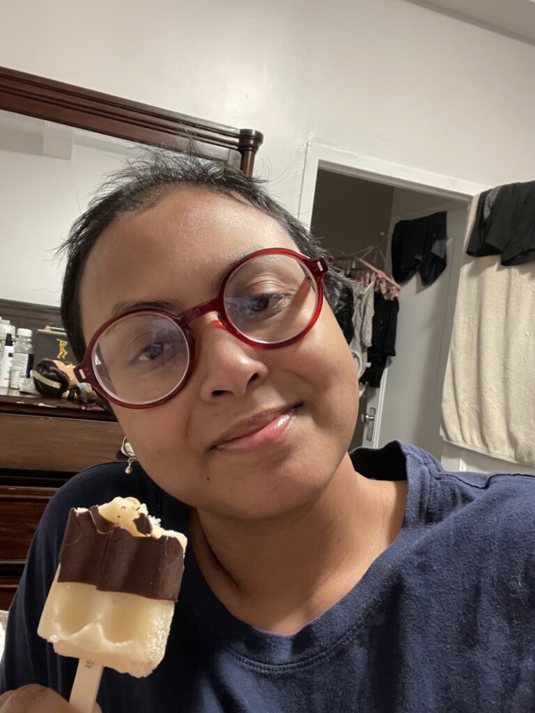 A woman with glasses holding up a piece of cake.