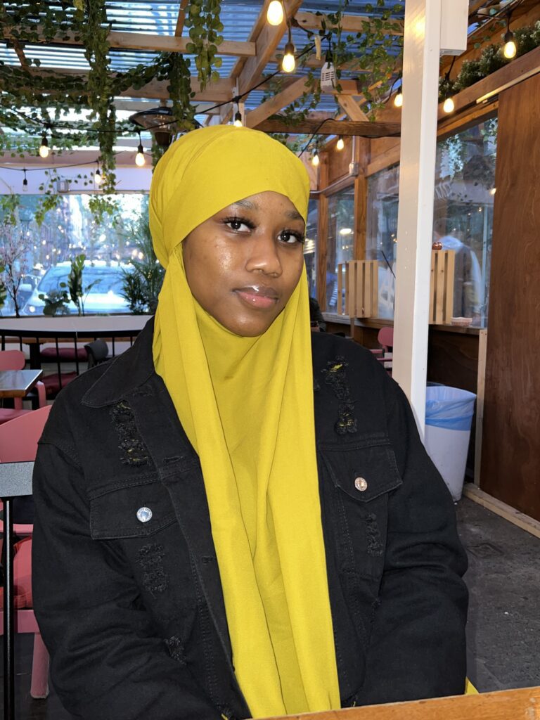 A woman wearing a yellow headscarf and black jacket.