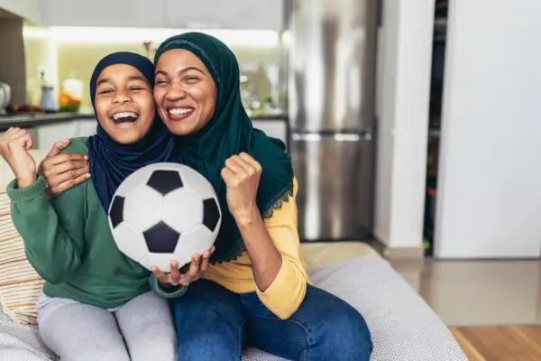 Two women sitting on a couch with a soccer ball.