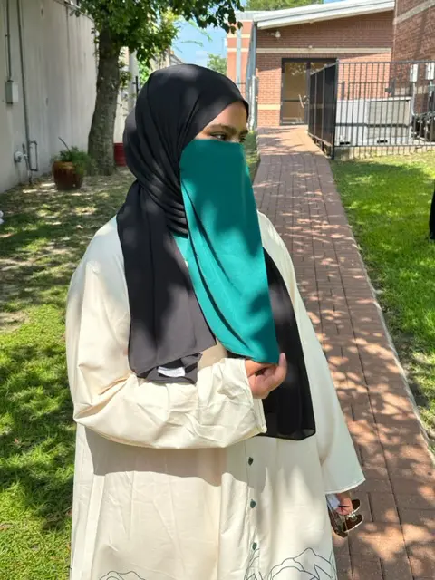 A woman in a hijab standing on the side of a walkway.