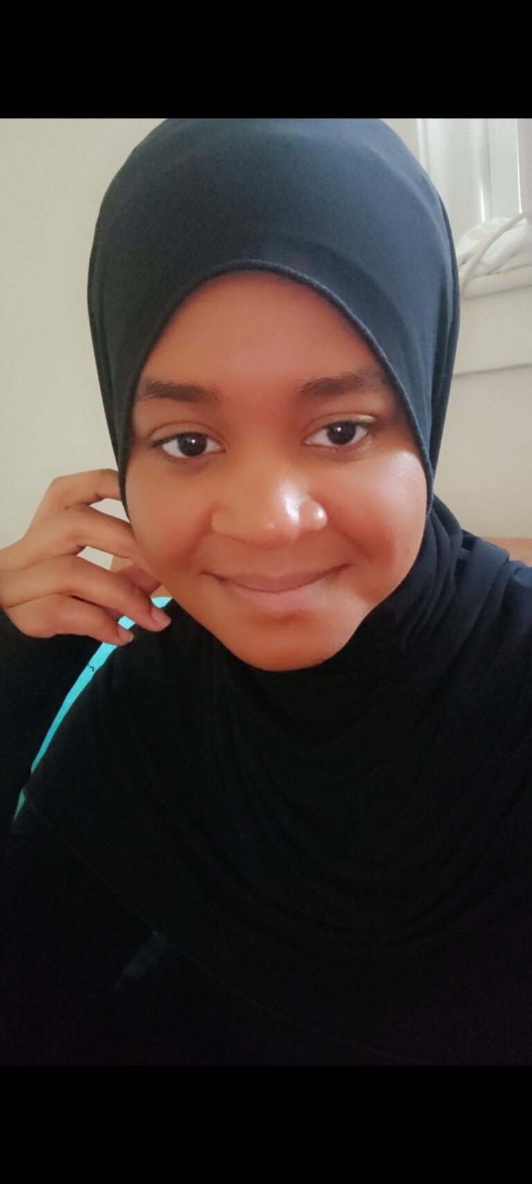 A young girl wearing a hijab and holding a phone.