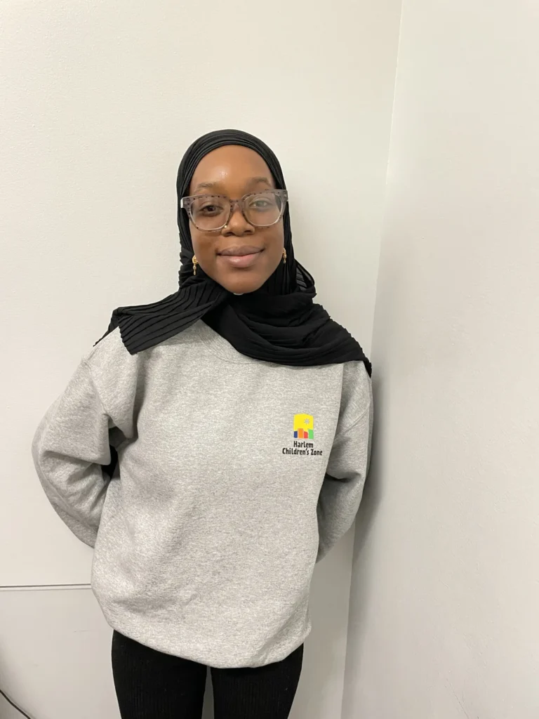 A woman wearing glasses and a hijab standing next to a wall.