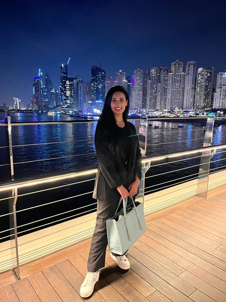 A lady standing on a wooden deck with the city skyline in the background and water.