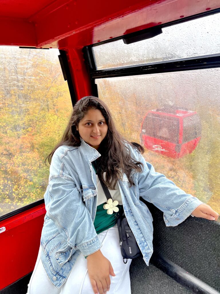 Woman smiling inside a cable car with autumn foliage outside.