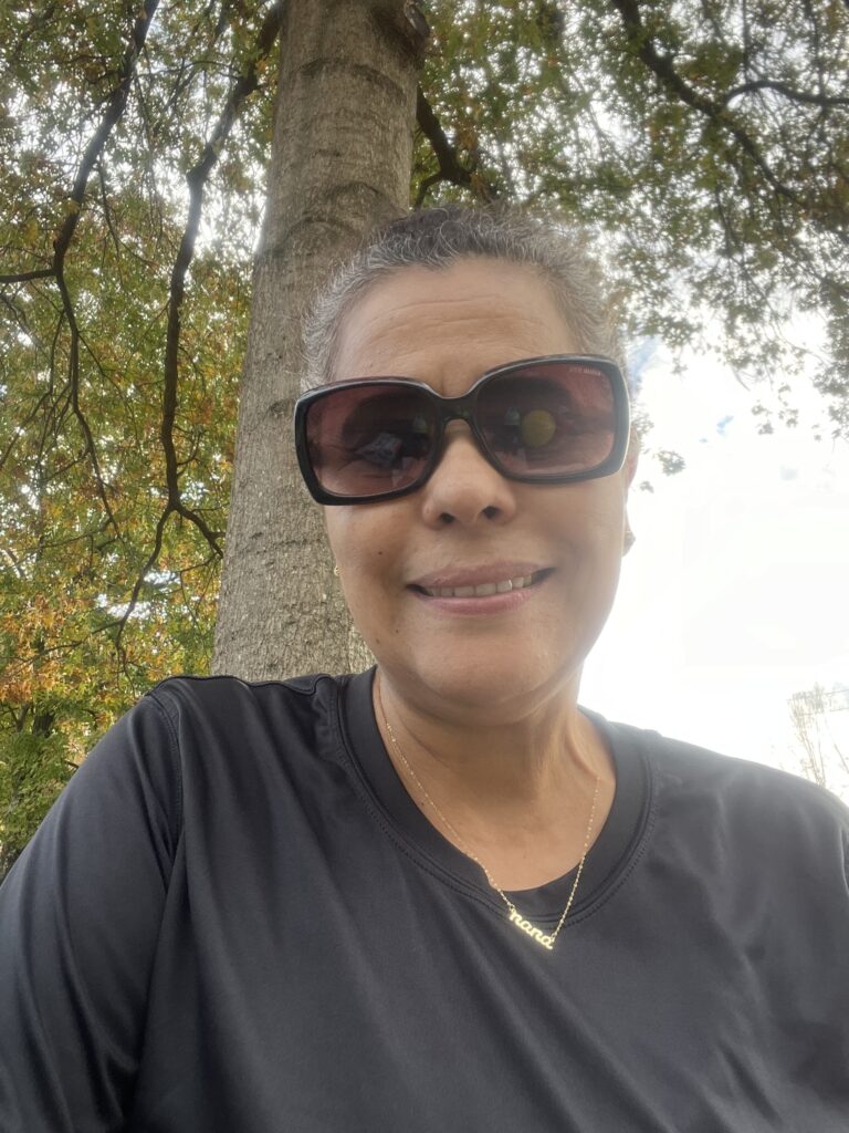 Smiling woman wearing sunglasses outdoors with trees in the background.