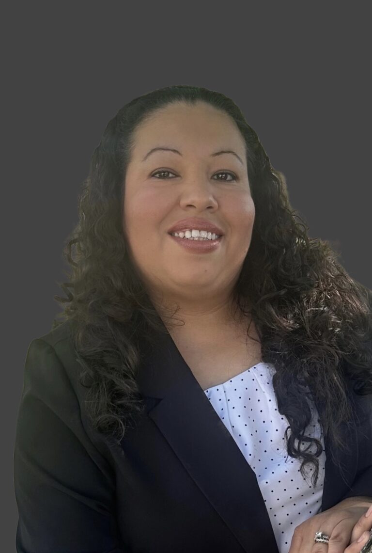 Smiling woman with curly hair wearing a dark blazer and white blouse.