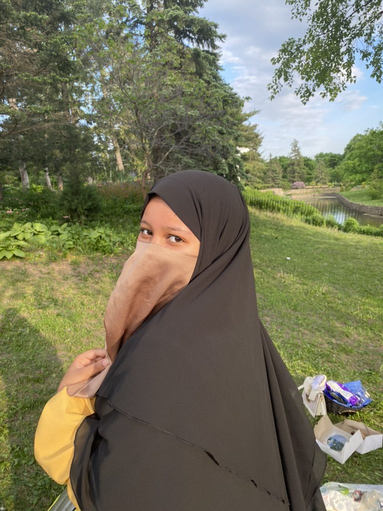 Woman wearing a black hijab outdoors in a green area.