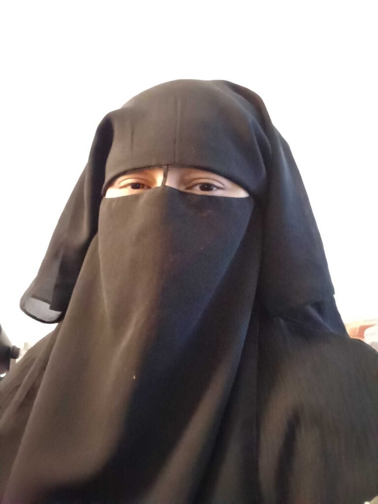 Person wearing a black niqab, white background.
