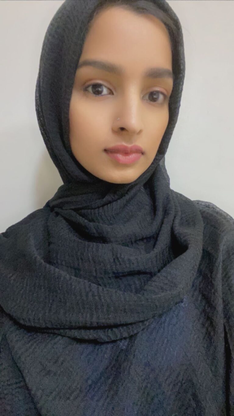 Woman wearing a black hijab, neutral background.