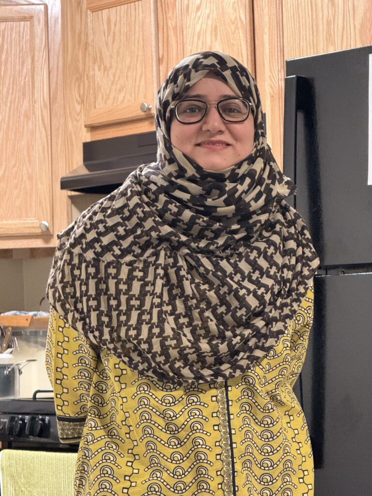 Smiling woman in patterned headscarf and glasses.
