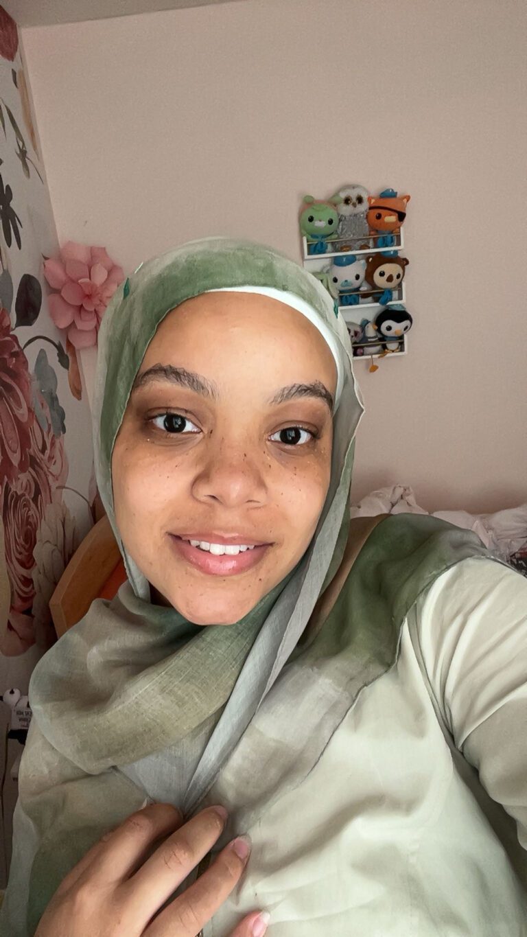 Woman smiling in green hijab, floral background.