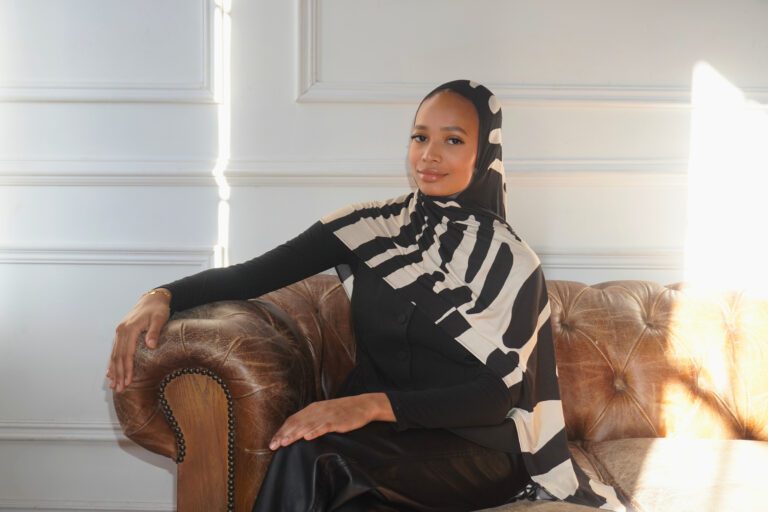Woman in patterned hijab sitting on sofa.