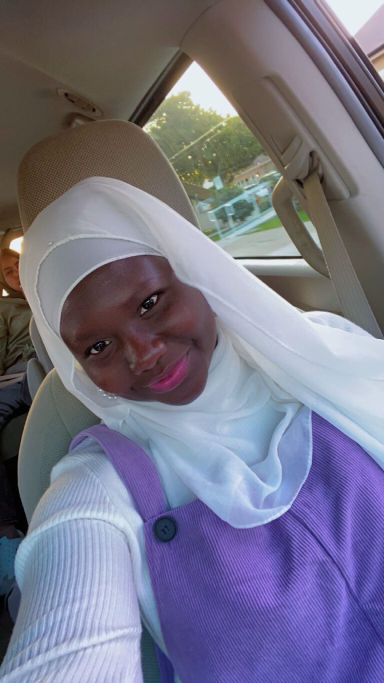 Woman in hijab smiling inside a car.