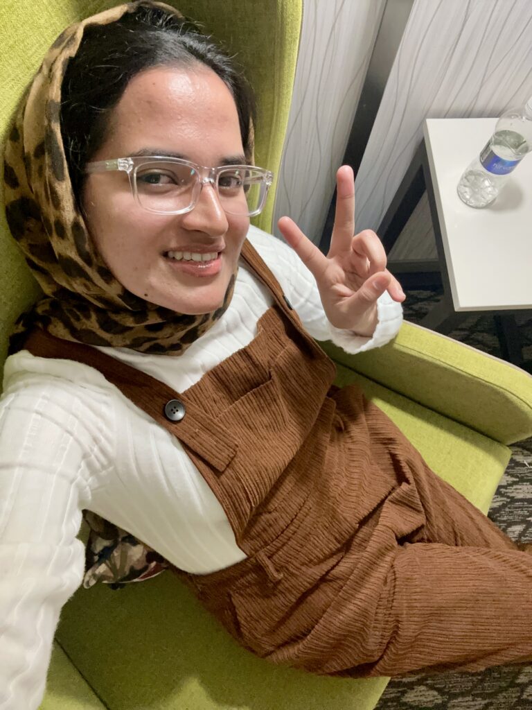 Woman sitting, smiling, giving peace sign.