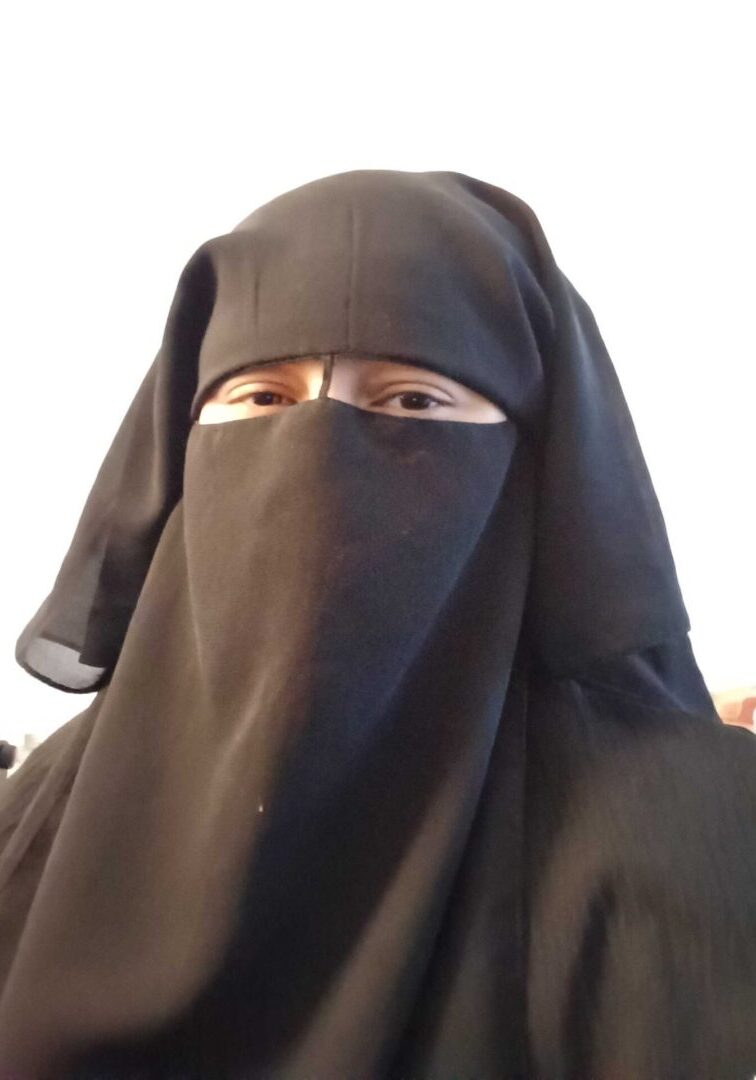 Person wearing a black niqab, white background.