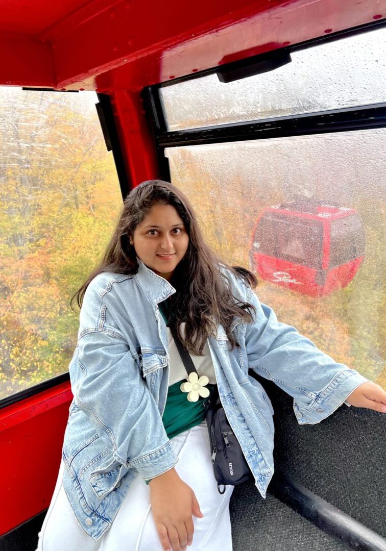 Woman smiling inside a cable car with autumn foliage outside.