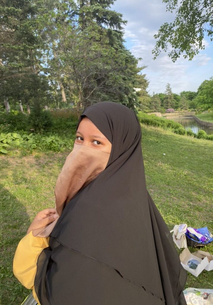 Woman wearing a black hijab outdoors in a green area.