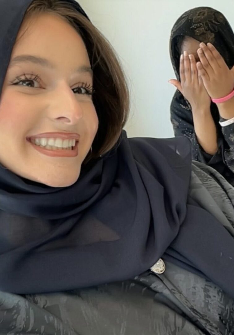 Two women in hijabs, one smiling, indoors.