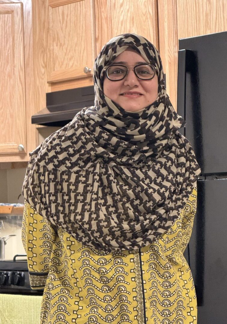 Smiling woman in patterned headscarf and glasses.