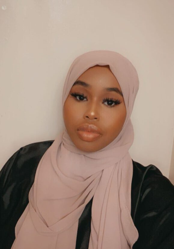 A woman wearing a light pink hijab and makeup, looking directly at the camera.